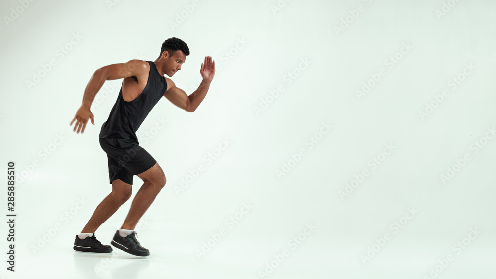 Full length of young african man with muscular body in sports clothing preparing to run in studio against grey background Full length of young african man with muscular body in sports clothing preparing to run in studio against grey background