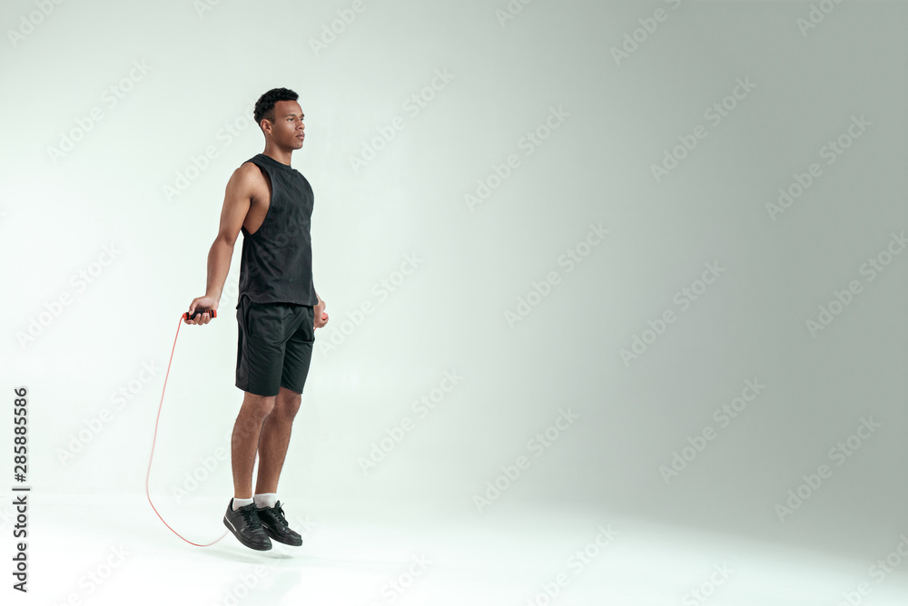 New champion. Full length of young african man in sport clothing skipping rope while exercising in studio against grey background New champion. Full length of young african man in sport clothing skipping rope while exercising in studio against grey background