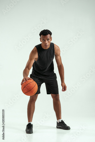 Great game. Full length of young african man in sports clothing playing basketball in studio against grey background © Friends Stock