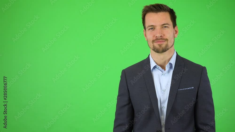 A young handsome businessman smiles at the camera and double clicks at a particular spot - green screen studio