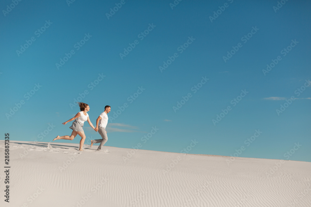 Fototapeta premium Romantic couple in love running on white sand in desert