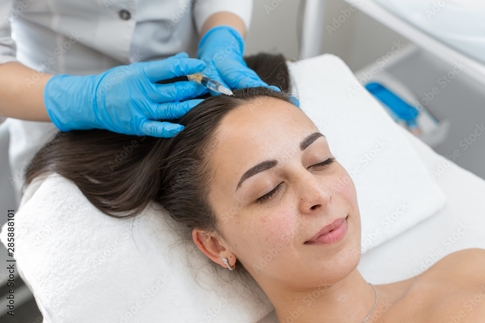 Beautician injections for healthy hair growth. Mesotherapy of the scalp. A young girl is undergoing a course of spa treatments in the office of a beautician. Moisturizing Beautician injections for healthy hair growth. Mesotherapy of the scalp. A young girl is undergoing a course of spa treatments in the office of a beautician. Moisturizing
