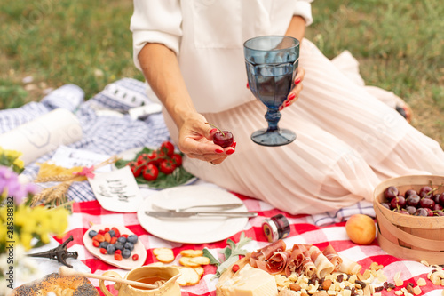 Girl holds juicy ripe cherries in her hand against the background of a checkered picnic blanket with food spread on it