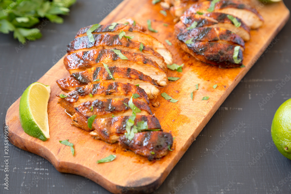 Grilled chipotle chicken breast on a rustic wooden board on a black surface, side view. Close-up. Grilled chipotle chicken breast on a rustic wooden board on a black surface, side view. Close-up.