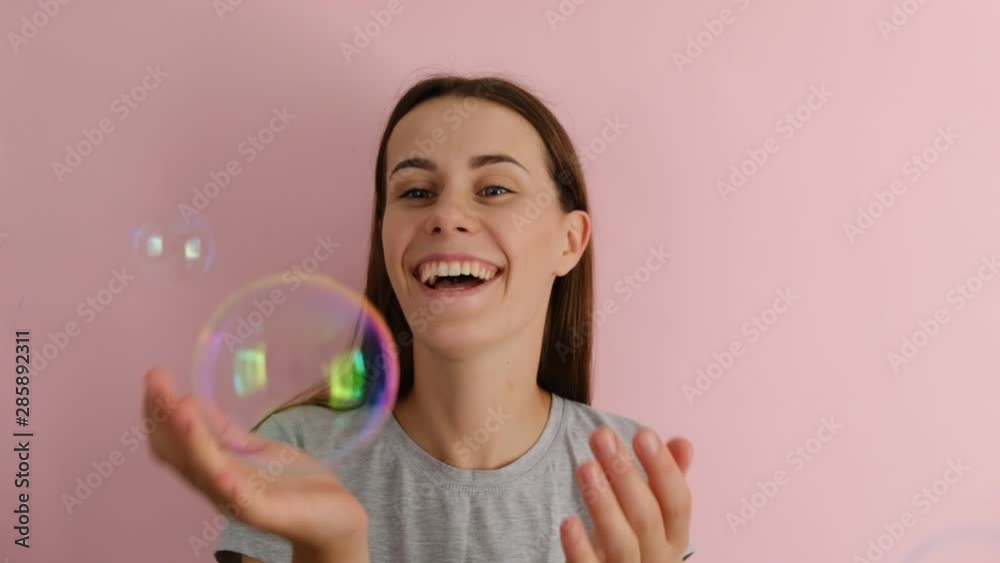 Beautiful young funny girl playing with bubbles isolated on the pink background. People and emotion concept Beautiful young funny girl playing with bubbles isolated on the pink background. People and emotion concept