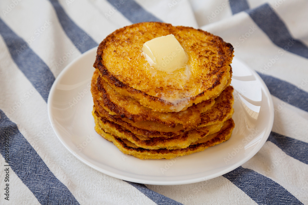 Homemade corn meal Johnny cakes with butter on a white plate, side view. Close-up. Homemade corn meal Johnny cakes with butter on a white plate, side view. Close-up.