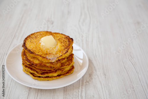 Homemade corn meal Johnny cakes with butter on a white plate over white wooden background, side view. Copy space.