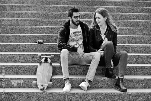 Cool multiracial couple sitting on stairs with longboard.