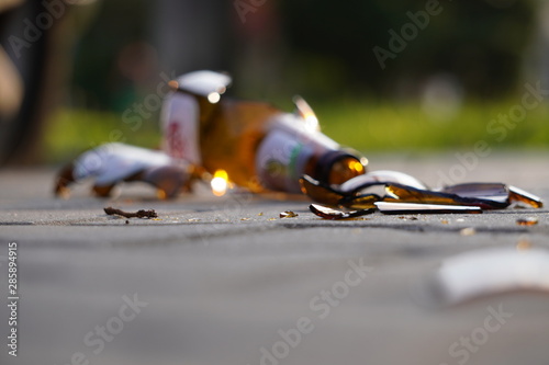 bottle of beer, soda or drugs from dark glass is broken. Shattered beer bottle on ground in sunset light. Fragments of glass on asphalt. Texture, background, wallpaper.
