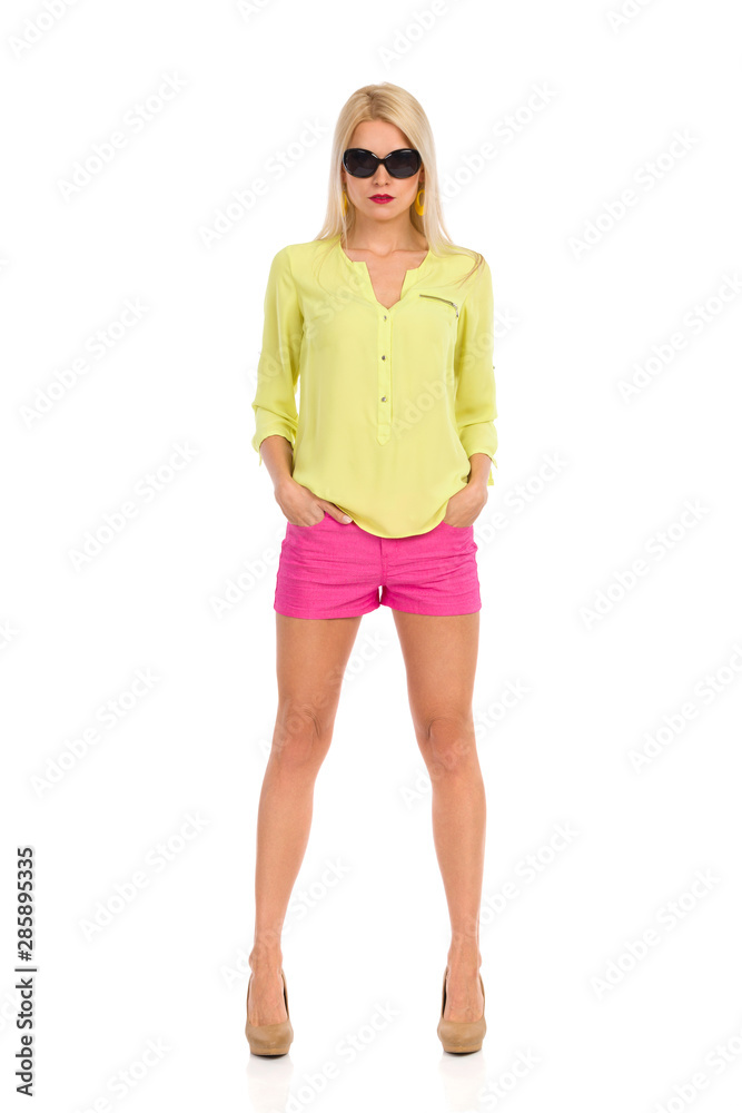 Fototapeta premium Serious Beautiful Blond Woman In Sunglasses Is Standing With Hands In Pockets. Front View.