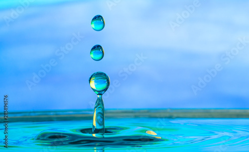 close up of a water drop impacting a body of water on a blue background