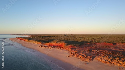 Scenic panoramic aerial drone view of outback landscape in remote Western Australia, flying along ocean, rocky cliff coast, with blue sky, sunset and horizon on a summer sunny day.