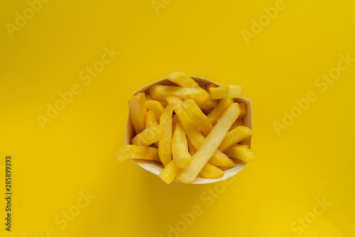 fresh fried junk potato fries come out from the paper box on color background