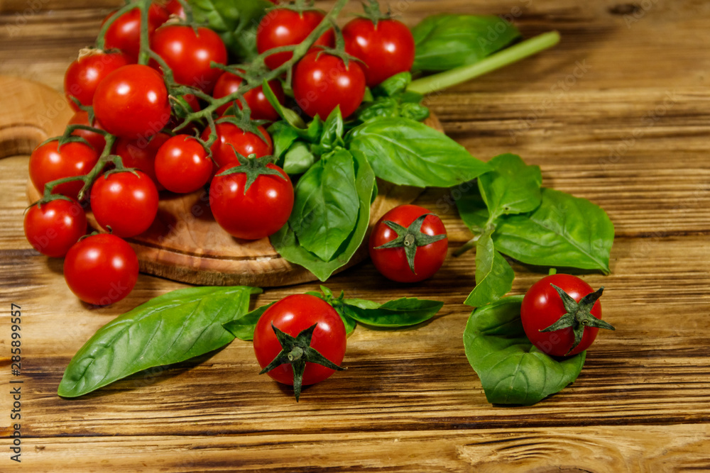 Fresh cherry tomatoes with green basil leaves on a wooden table Fresh cherry tomatoes with green basil leaves on a wooden table