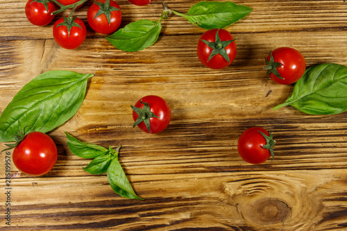 Fresh cherry tomatoes with green basil leaves on a wooden table. Top view