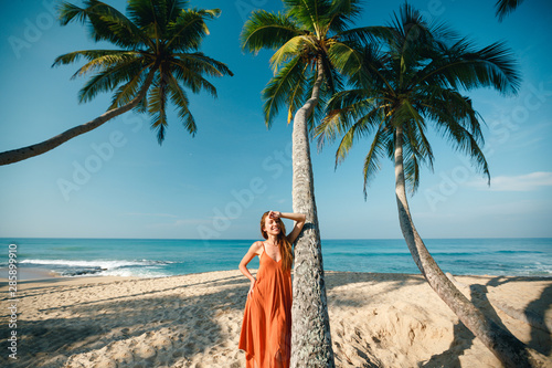 Vacation concept, happy young woman smiles, in the summer against a backdrop of palm trees and ocean. Portrait of carefree girl  joy and laughing while standing  near palm tree photo