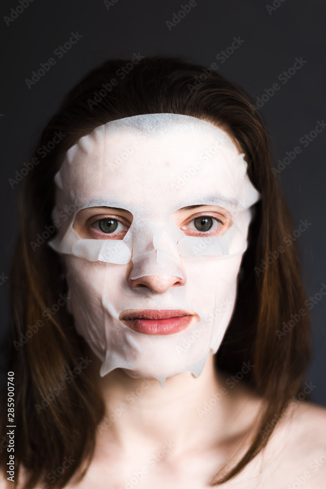 Face of a young woman with a tissue moisturizing cosmetic mask - cosmetic procedures