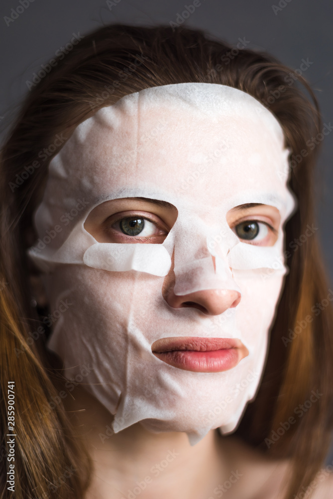 Face of a young woman with a tissue moisturizing cosmetic mask - cosmetic procedures