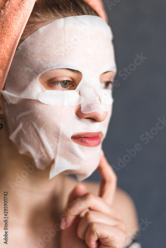 Face of a young woman with a tissue moisturizing cosmetic mask - cosmetic procedures