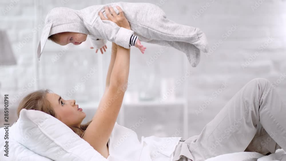 Charming young mother playing with little cute baby holding over head having positive emotion
