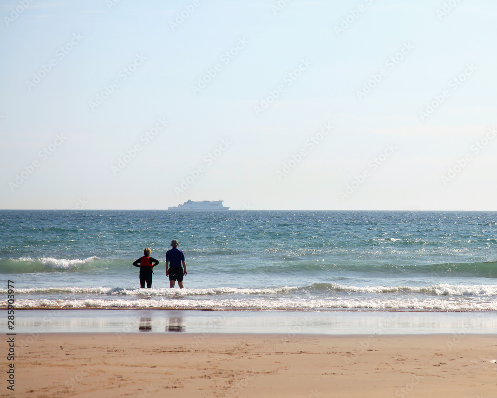Couple on a beach watching a ferry go past