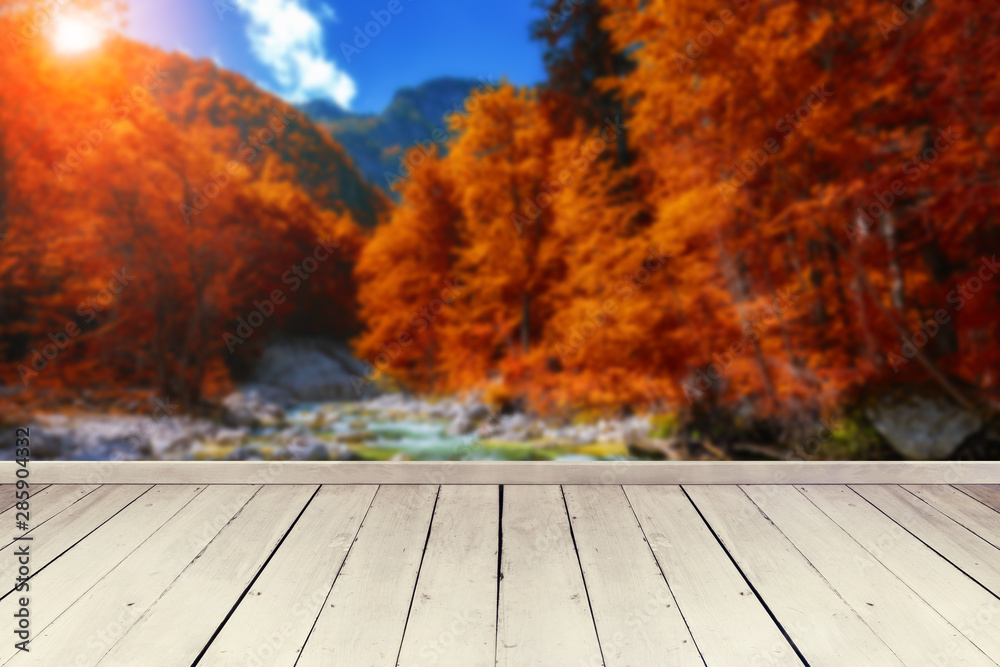 Empty wooden table for product placement or montage with focus to table top in the foreground, blurred autumn landscape in the background with waterfall and mountains.