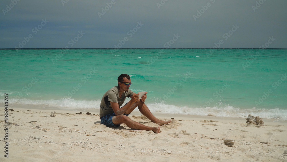 A man with a tablet on a tropical beach on a sunny day. Summer and travel vacation concept. A man with a tablet on a tropical beach on a sunny day. Summer and travel vacation concept.
