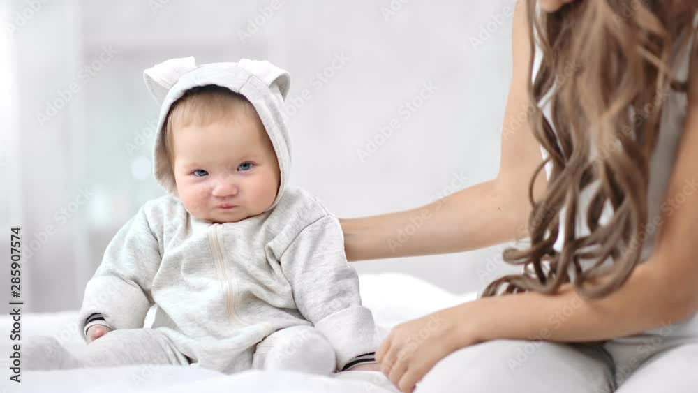 Smiling baby wearing cute overall sitting on bed having positive emotion looking at camera Smiling baby wearing cute overall sitting on bed having positive emotion looking at camera