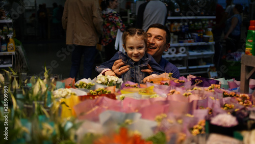 Portrait of cute little girl choosing flowers in supermarket with happy dad