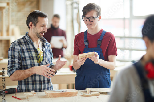 Waist up portrait of mature carpenter talking to smiling young apprentice in workshop, copy space photo