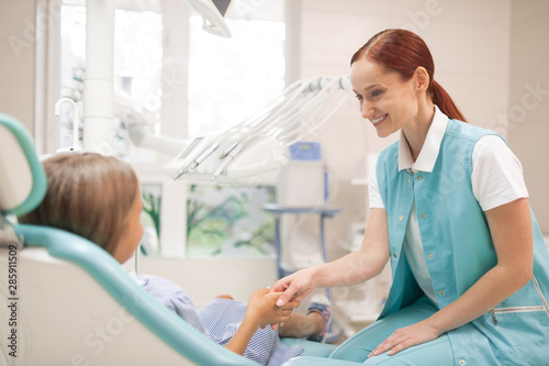 Red-haired dentist smiling and shaking hand of her client