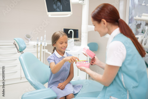 Child dentist giving girl a lesson of teeth brushing
