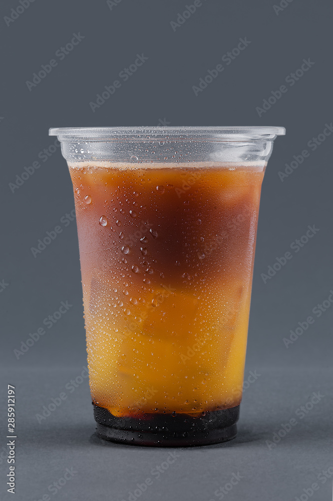 Cold drink with coffee, orange juice and ice cubes on a gray background