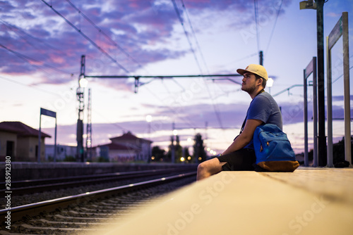Young man with a backpack and cap sitting near the tracks.