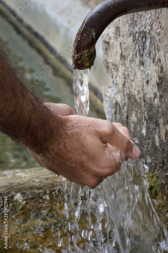Manos de hombre recogiendo agua de una fuente de piedra.
