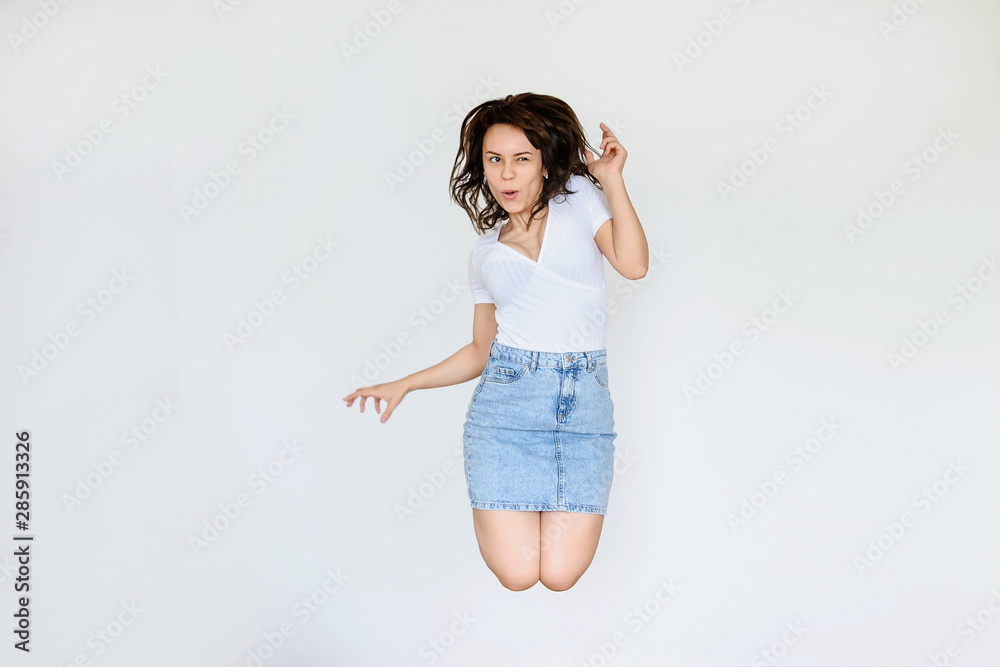 close up photo of a happy brunette in white blouse and denim skirt jumping in the air close up photo of a happy brunette in white blouse and denim skirt jumping in the air