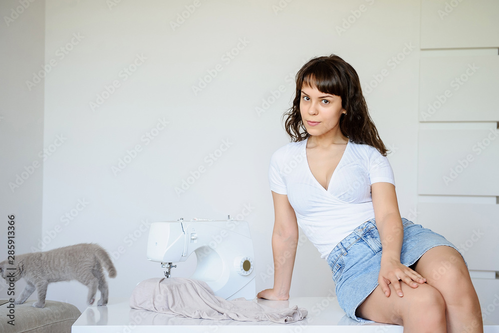 close up photo of a sexy brunette sitting near a white sewing machine and playing with a gray kitten close up photo of a sexy brunette sitting near a white sewing machine and playing with a gray kitten