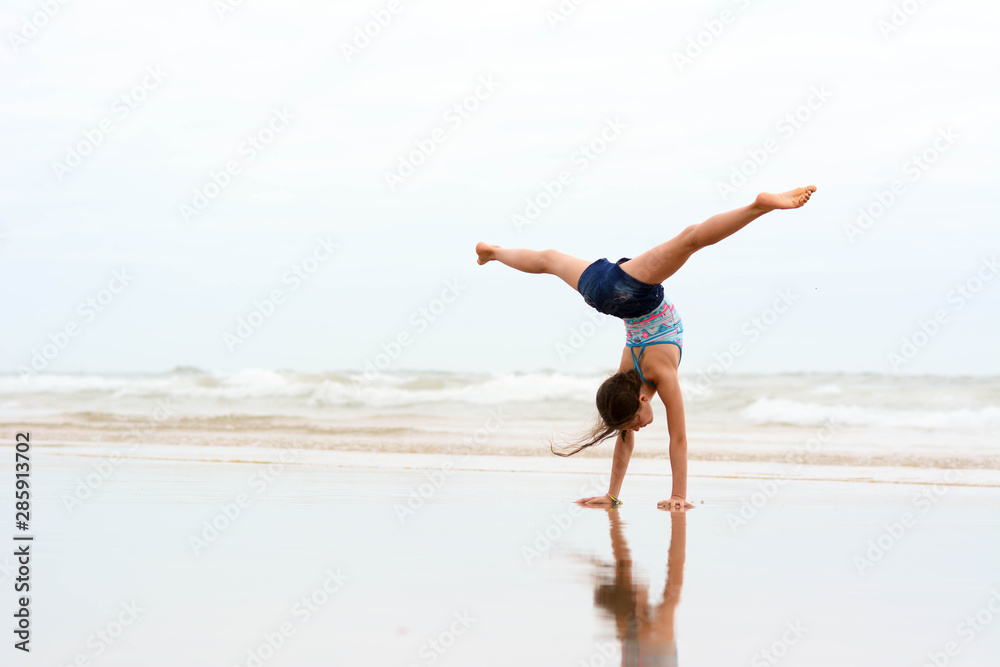 Sport, training, fitness, yoga, active lifestyle concept. Flexible girl gymnast doing acrobatic exercise at the beach.