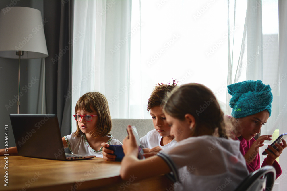 Childhood, technology and family concept - little girls and boy with tablet and smartphones in the kitchen at home. Childhood, technology and family concept - little girls and boy with tablet and smartphones in the kitchen at home.