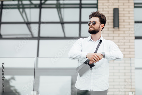 Portrait of a young handsome stylish guy in a white shirt on the streets of the city in sunglasses. Copy space. Blurred background.