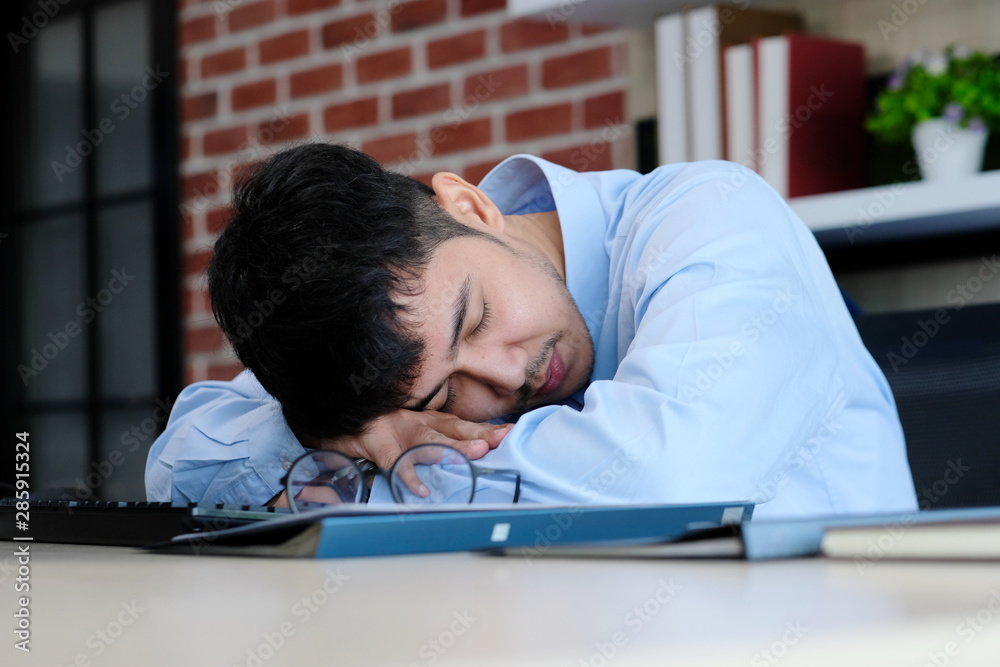Tired asian man sleeping at office desk. Young businessman with eyeglasses overworked and fell asleep, Creative casual man sleeping at his working place Tired asian man sleeping at office desk. Young businessman with eyeglasses overworked and fell asleep, Creative casual man sleeping at his working place