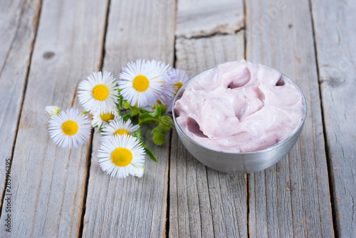 pink cosmetic cream and white herbal flowers on old rusty wooden table background