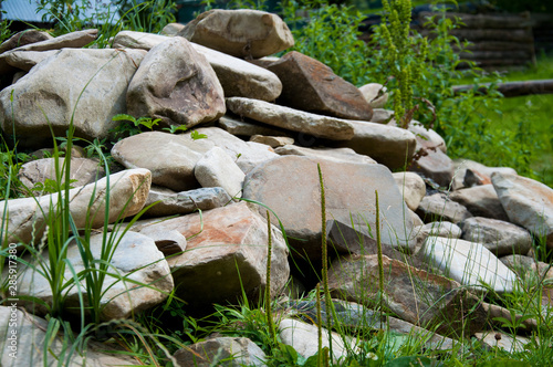 Green grass grows near a large pile of stones. Summer