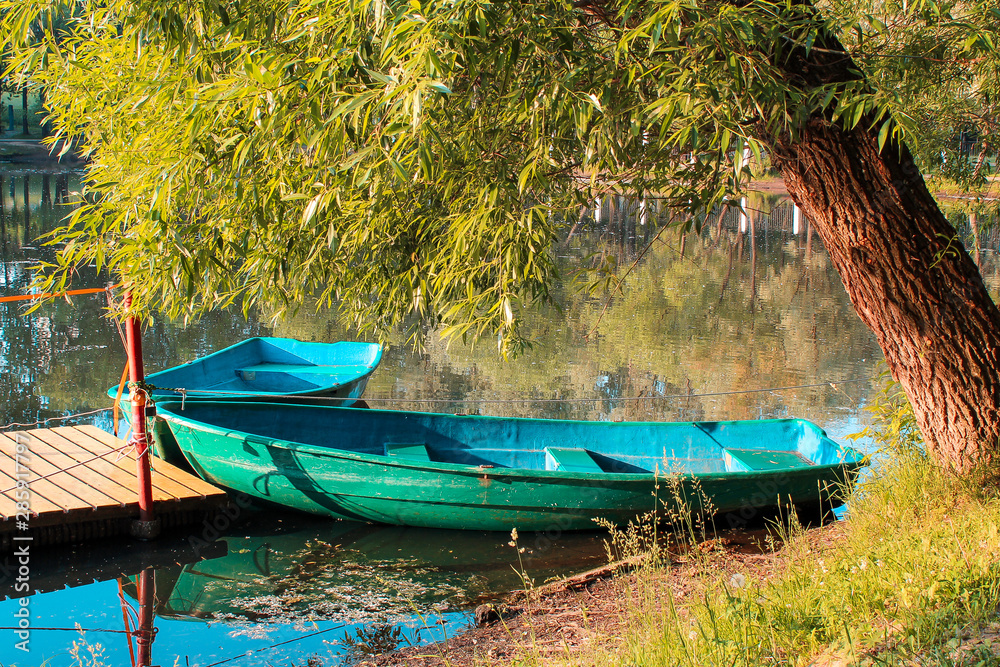 Two boats on the water. Two wooden boats in a pond under a tree in the setting sun Two boats on the water. Two wooden boats in a pond under a tree in the setting sun