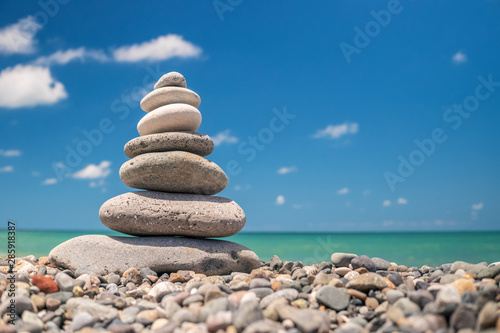 Pebble pyramid on the beach on a background of blue sky with clouds on a sunny day. The concept of harmony of balance and meditation. copy space