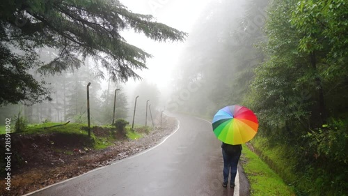 Young indian woman standing on a fog covered street with a colorful umbrella in Mcleodganj dharamshala India on an adventure trip or vacation photo