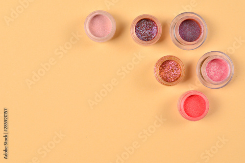 Cosmetics. Makeup. Jars with crumbly bright shadows, glitter. Pink,peach, golden colors on beige background. Closeup. Space for text or design.