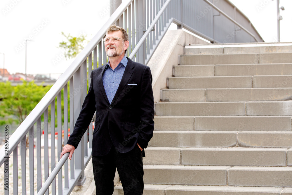 handsome businessman smiling and standing by stairs
