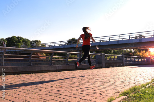 Young attractive sporty fitness woman running while exercising outdoors at sunset or sunrise.