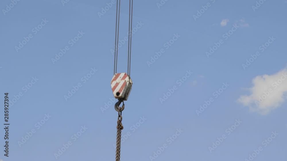 Crane hook with red and white stripes hanging, blue sky in background. Crane hook with red and white stripes hanging, blue sky in background.
